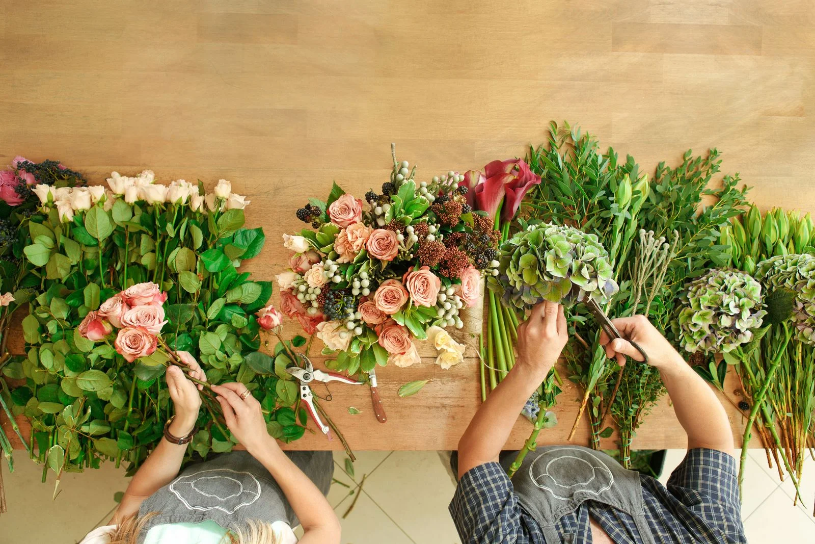 Two florists arranging flowers and greenery at a work table.