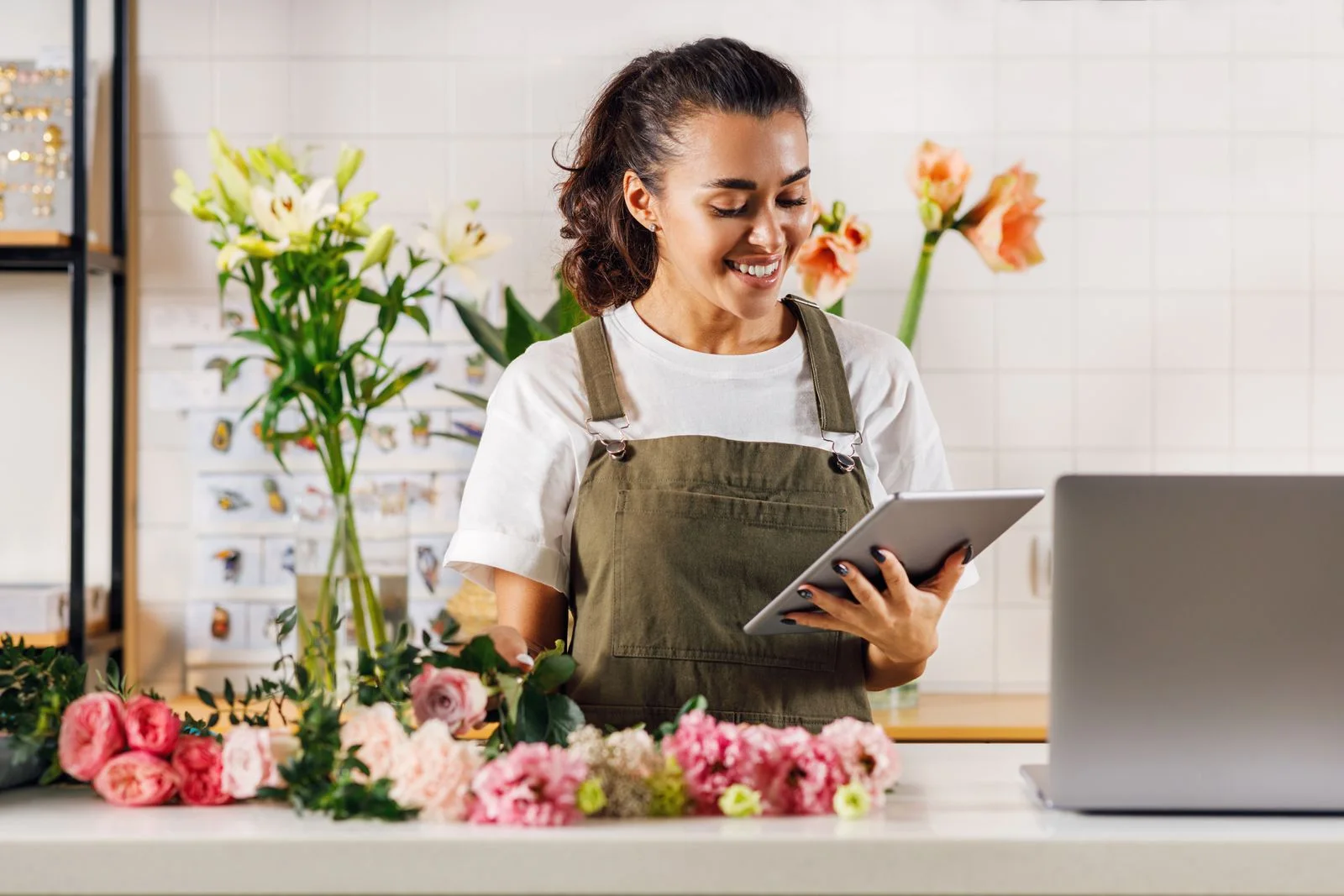 Florist using a tablet in a flower shop surrounded by colorful flowers.